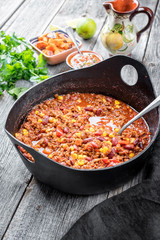 Traditional slow cooked Mexican chili con cane with mincemeat, beans and corn as top view in a modern design cast-iron roasting dish