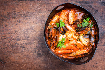 Traditional Catalan fish stew romesco de peix with prawns, mussels and fish as top view in a modern...