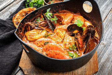 Traditional Catalan fish stew romesco de peix with prawns, mussels and fish as closeup in a modern...