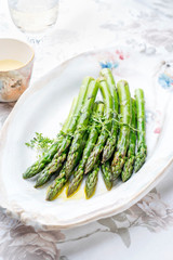 Traditional boiled green asparagus with butter sauce decorated with cress as closeup on a design plate