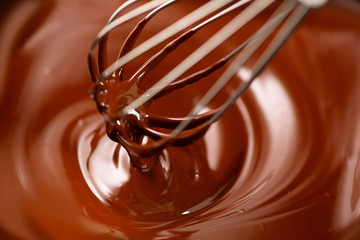 Chocolate. Mixing melted dark chocolate with a whisk. Closeup of liquid hot chocolate swirl....
