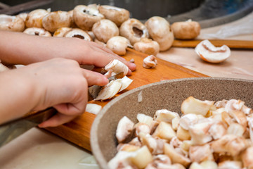 Children's small hands, a knife, shampions and a frying pan. The child cuts champignons.