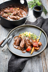 Traditionelle geschmorte Schweinebäckchen in brauner Rotwein Sauce mit Pilzen und Kartoffelpüree als closeup auf einem Modern Design Teller