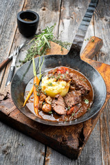 Traditionelle deutsche geschmorte Schweinebäckchen in brauner Rotwein Sauce mit Kartoffel Püree und Pilzen als closeup in einer schmiedeeisernen Pfanne