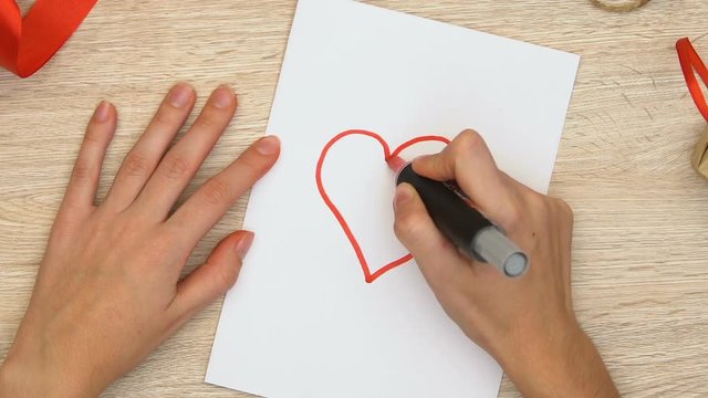 Woman drawing red heart on white paper, charity and donations concept, top view