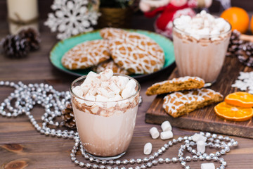 Hot cocoa with marshmallows in glasses and christmas cookies on a plate on the wooden table in Christmas decorations