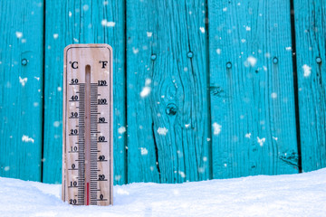 Wooden thermometer on a background of green boards and white snow