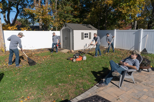 The same man performing many landscaping jobs to rake leaves and clean back yard in autumn fall cleanup appearing to work as single team in multiple exposure photography effect humor funny view