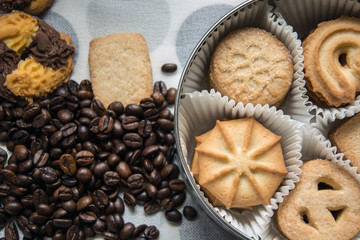 Cookies with sugar in a round box and coffee beans sprinkled on a tablecloth