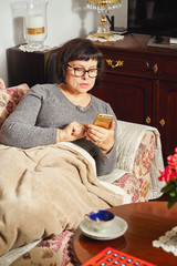 attractive elderly woman lying on the couch and surfing the internet at home.