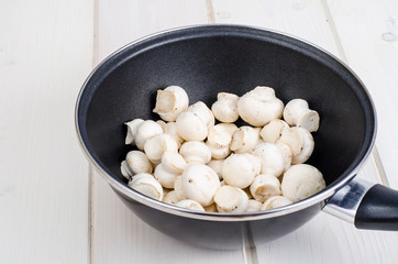 White fresh  champignons in pan on wooden kitchen table. Concept of cooking mushroom dishes