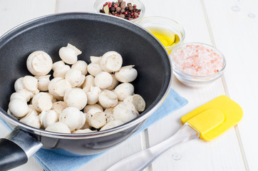 White fresh  champignons in pan on wooden kitchen table. Concept of cooking mushroom dishes