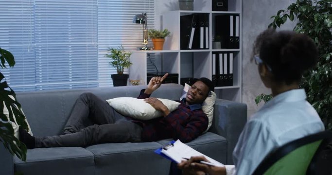 Medium shot of young man lying on a couch while talking to a psychologist