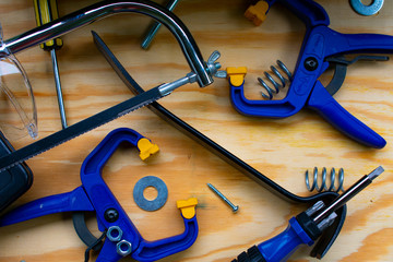 Tools Including Bar Clamps, Crow Bar, Screwdriver, Screw, Nut, Washer, and Hacksaw Against Plywood