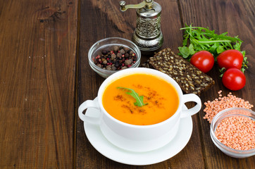 Red lentil soup in plate on wooden background