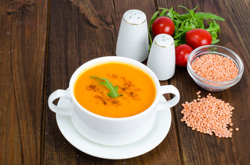 Red lentil soup in plate on wooden background