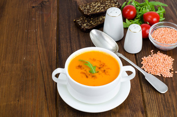 Red lentil soup in plate on wooden background