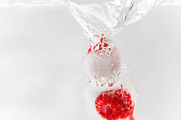 Two frozen raspberries falling into water. Washing berries