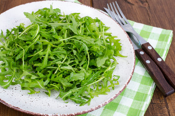 Vegetarian dish, plate with green arugula on wooden table