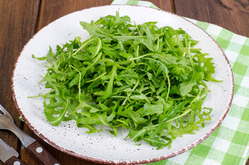 Vegetarian dish, plate with green arugula on wooden table