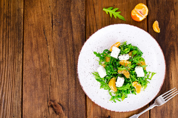 Delicious fruit and vegetables salad. Tangerine, feta cheese, arugula and chia seeds in plate. Healthy food concept