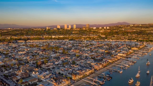 Aerial view and time lapse over Newport Beach harbor and coastal Orange County in California at sunset with boats and neighborhood beach homes below.