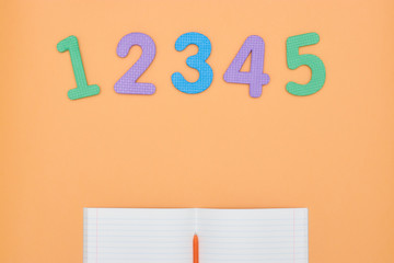 Notebook, pen and colored numbers on orange background. Accessories for study. Top view, flat, copy...