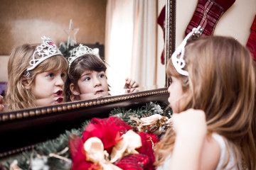 Two adorable, cute girls, sisters, twins with tiaras, looking in the mirror