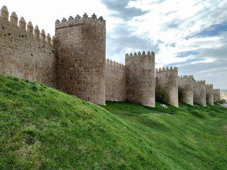 Fototapeta na wymiar The wall of Avila, Spain. The stone wall with its turrets behind a green lawn.