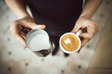 Barista holds two cups, with milk and latte