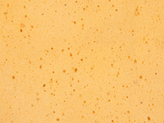 The texture and bubbles on the surface of a yellow sponge are shown in a closeup view.