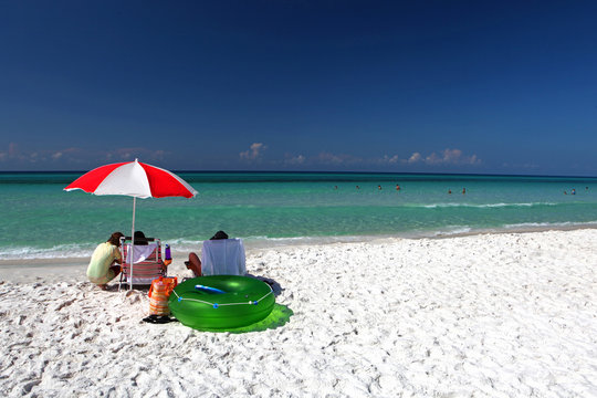 A family sits under an umbrella on a sandy beach in the Florida panhandle.