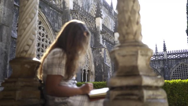 Side view crop young lady with pen and notebook sitting near column inside old abbey in Portugal