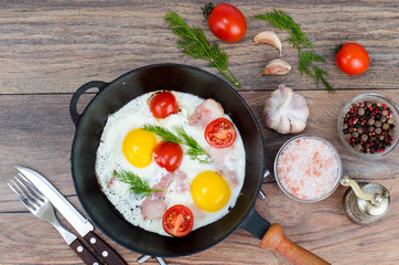 Frying pan with fried eggs, bacon and tomatoes