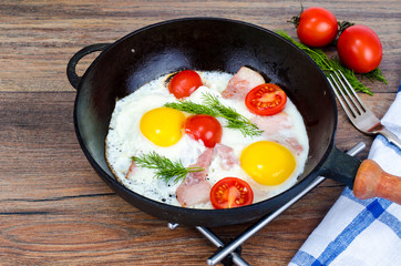 Frying pan with fried eggs, bacon and tomatoes