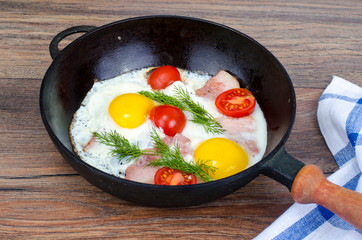 Frying pan with fried eggs, bacon and tomatoes