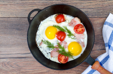 Frying pan with fried eggs, bacon and tomatoes