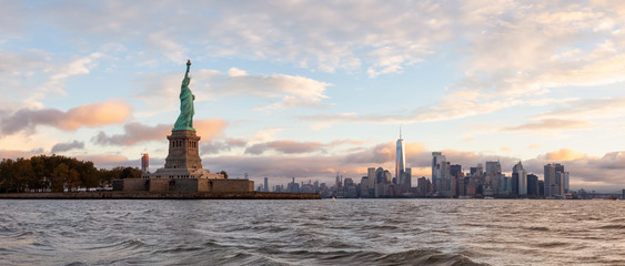 Panoramic view of the Statue of Liberty and Downtown Manhattan in the background during a vibrant cloudy sunrise. Taken in Jersey City, New Jersey, United States. © edb3_16
