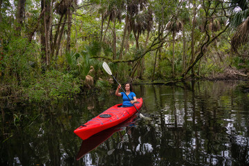 Adventurous girl kayaking on a river covered with trees. Taken in Chassahowitzka River, located...