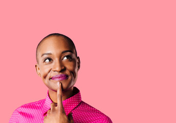 Fototapeta Portrait of a young woman in pink shirt with finger on mouth looking up thinking, isolated on pink studio background obraz