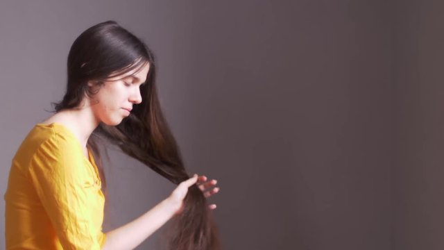 Young girl in yellow t-shirts and big glasses is combing her very long hair. Raises and releases hair.