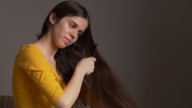 Young girl in yellow t-shirts and big glasses is combing her very long hair. Raises and releases hair.