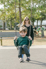 Mom Pushing Son Little Boy on the Swings at the Park Playground