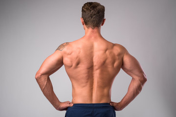 Rear view of muscular man shirtless with hands on hips