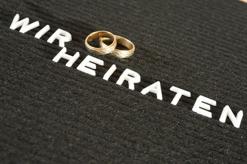 Fototapeta premium Zwei Eheringe und Slogan Wir heiraten