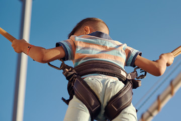 European boy is jumping on bungee trampoline in a Luna park. Back view.