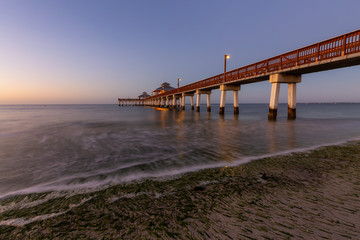 Fototapeta premium Beautiful view of a wooden Pier on the Atlantic Ocean during a vibrant sunrise. Taken in Fort Myers Beach, Florida, United States.