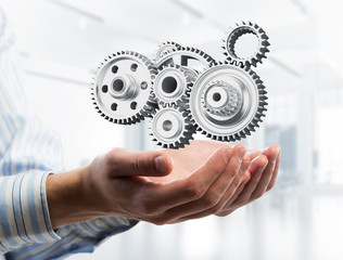 Engine mechanism in male ahnds as symbol for cooperation or teamworking. Mixed media