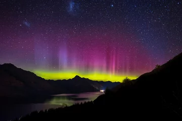 Fotobehang Spectacular view as aurora lights up the sky of Queenstown, New Zealand. When particles from a solar storm reached our Earth, it creates an array of colored lights as they hit the atmosphere. © Skyimages