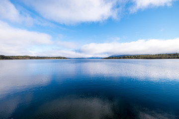 Fototapeta premium This is a photograph of a very blue lake. The water looks crystal clear. It has a perfect mirror image of the sky and trees.